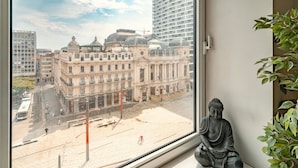 A Buddha statue on a windowsill with a view of a cityscape including historic buildings and a modern high-rise. - Deluxe 7-guest Apartment in Antwerp (Antwerp)