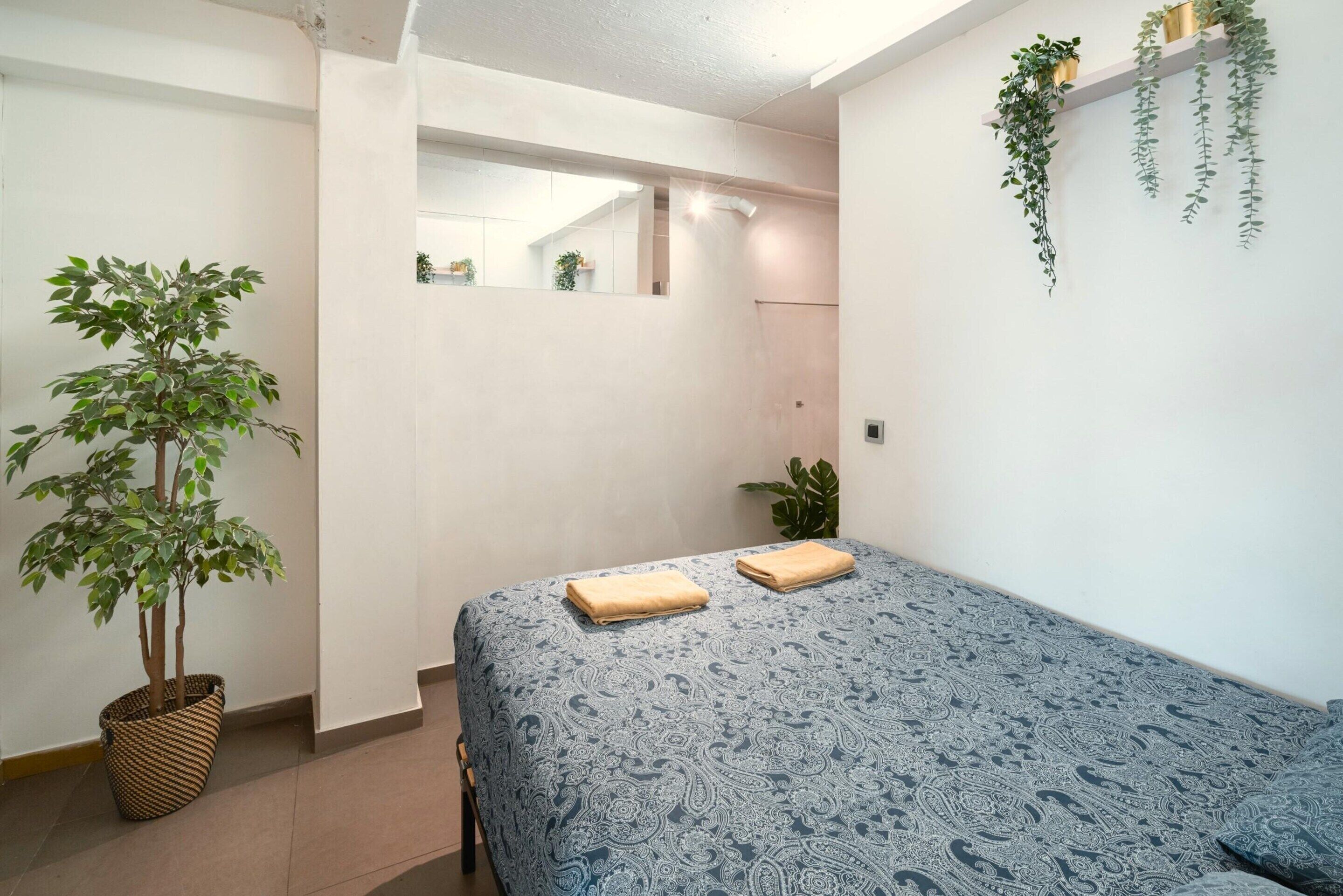 A bedroom with a bed, a potted plant, a mirror, and a hanging plant.