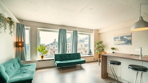 A modern living room with a sofa, a dining area with a bar, and large windows with curtains. - Deluxe 7-guest Apartment in Antwerp (Antwerp)