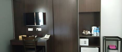 Habitación compacta con escritorio, silla, televisor de pantalla plana, refrigerador minibar y repisa con artículos de aseo.
