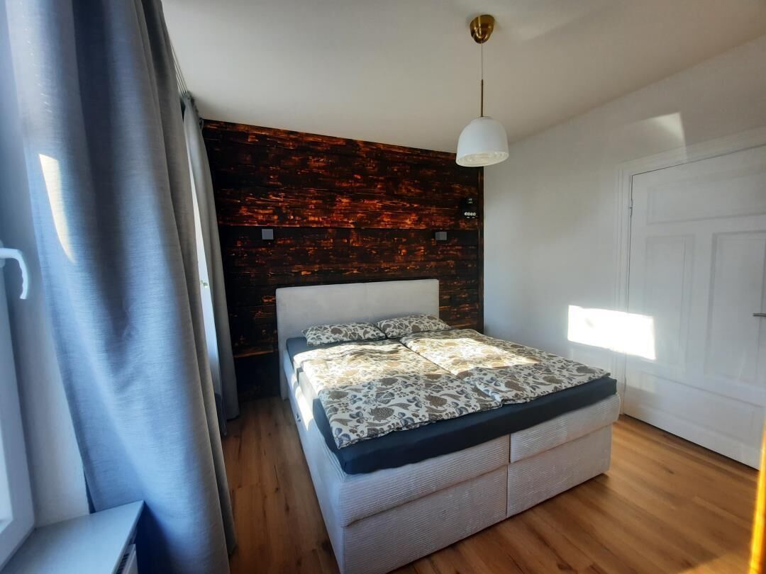 Ein modernes Schlafzimmer mit einem Bett, einer Holzwand, einer weißen Deckenleuchte und einer Tür.