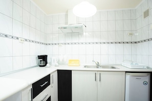 A kitchen with white tiles, a coffee maker, a sink, and a dishwasher.