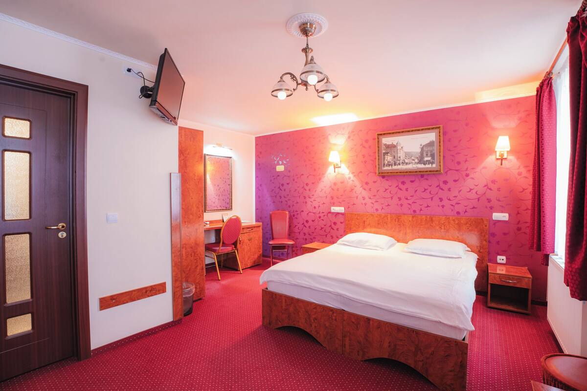 Una habitación de hotel con cama, escritorio, silla, televisor y lámpara.