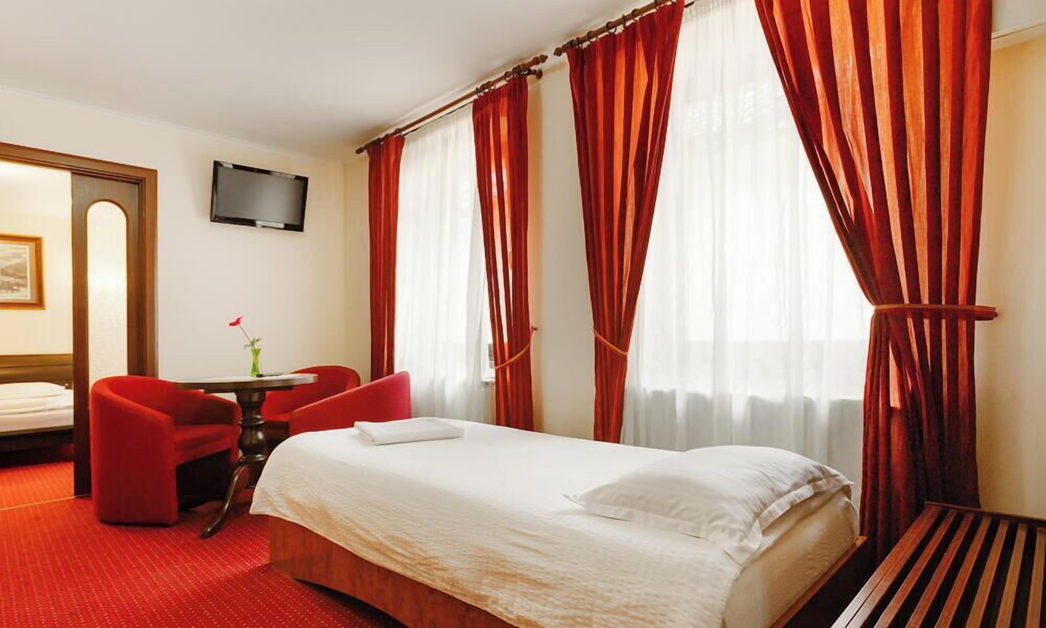 A hotel room with a bed, a desk, a chair, a TV, and red curtains.