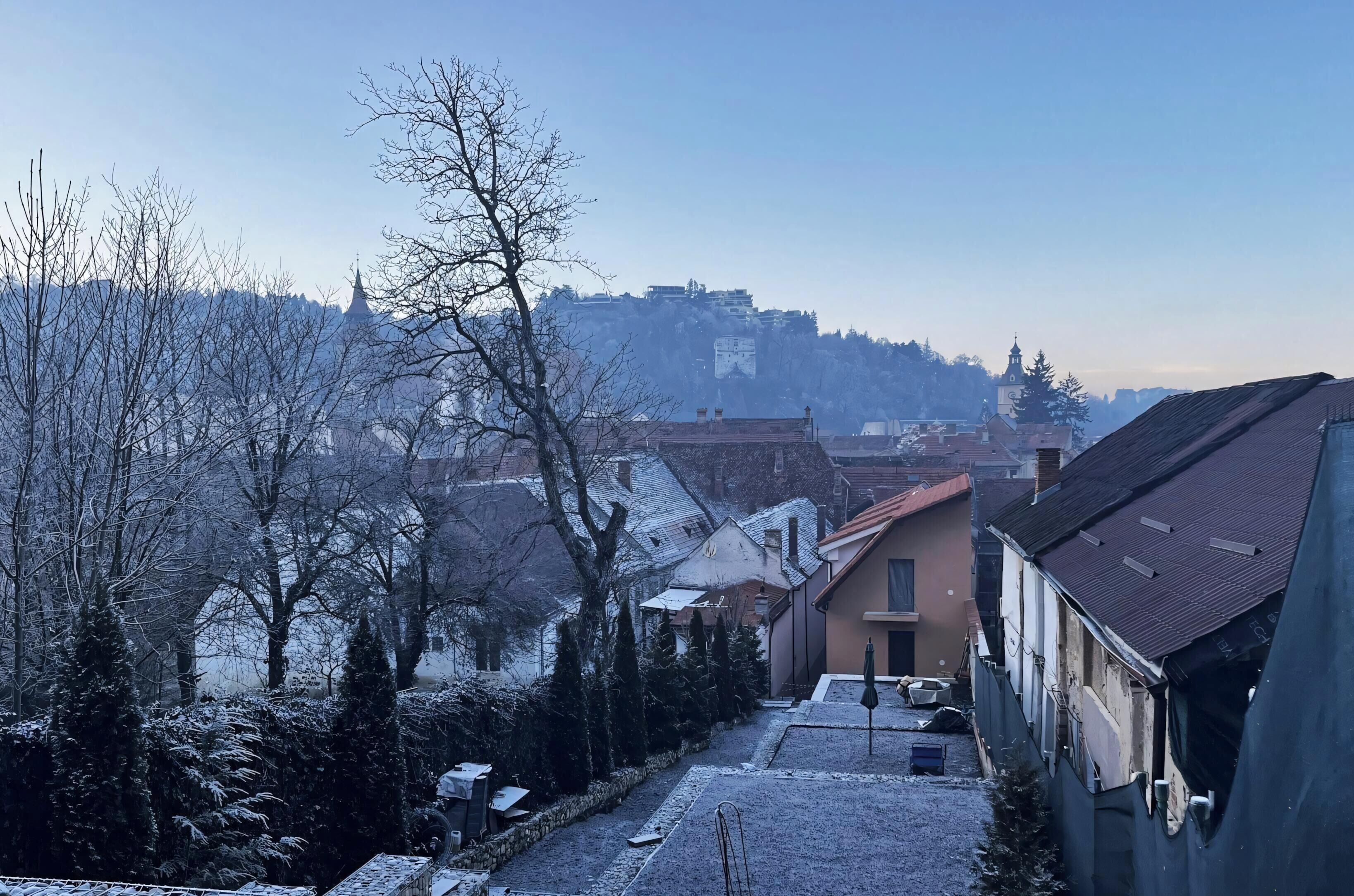 Un quartier résidentiel où les arbres et les maisons sont recouverts de neige, le ciel est dégagé et, au loin, on aperçoit une colline parsemée de bâtiments.