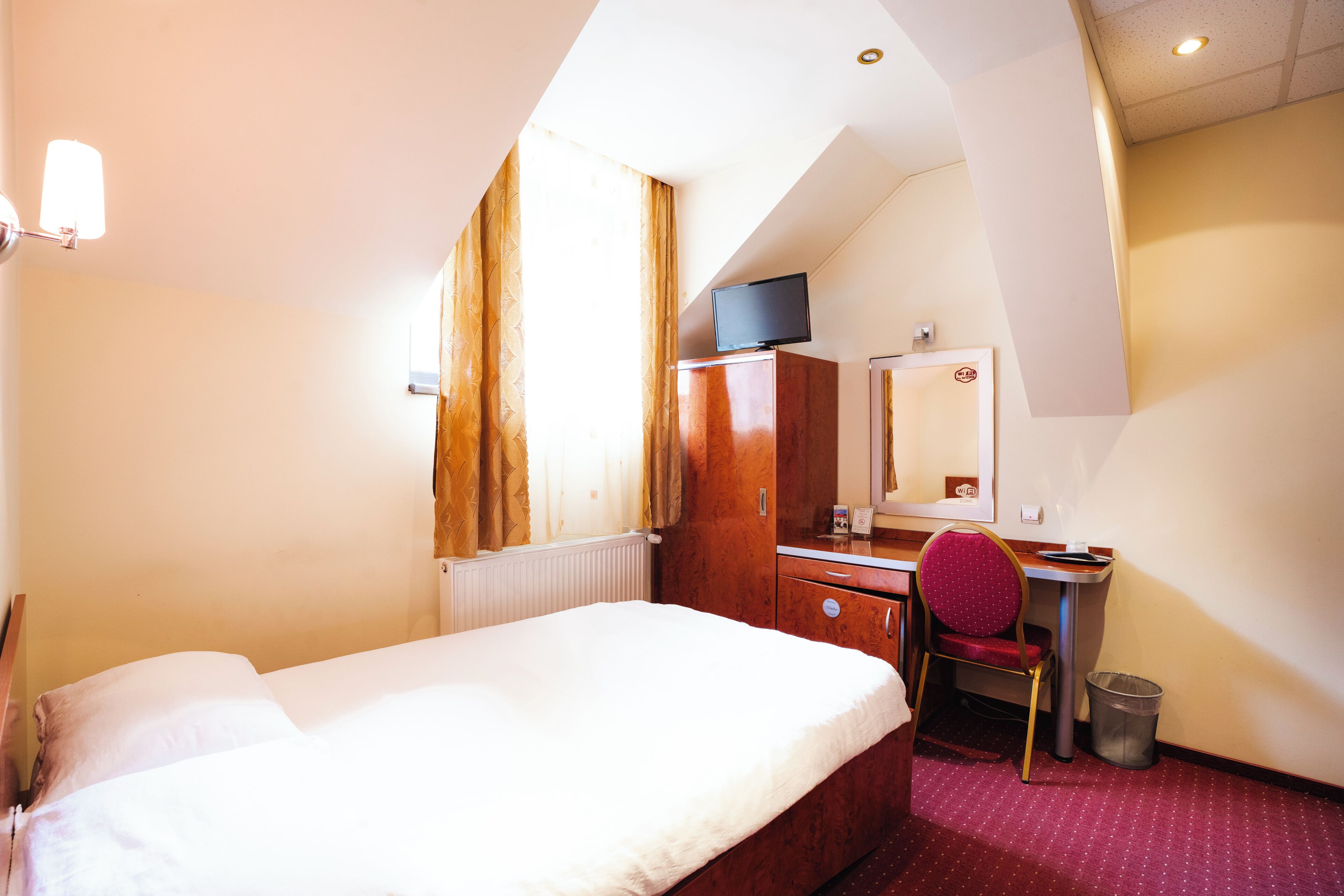 A hotel room with a bed, a desk, a chair, a television, and a window with curtains.