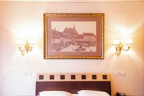A hotel room with a framed historical photo, wall sconces, a wooden headboard, and a bedside telephone.