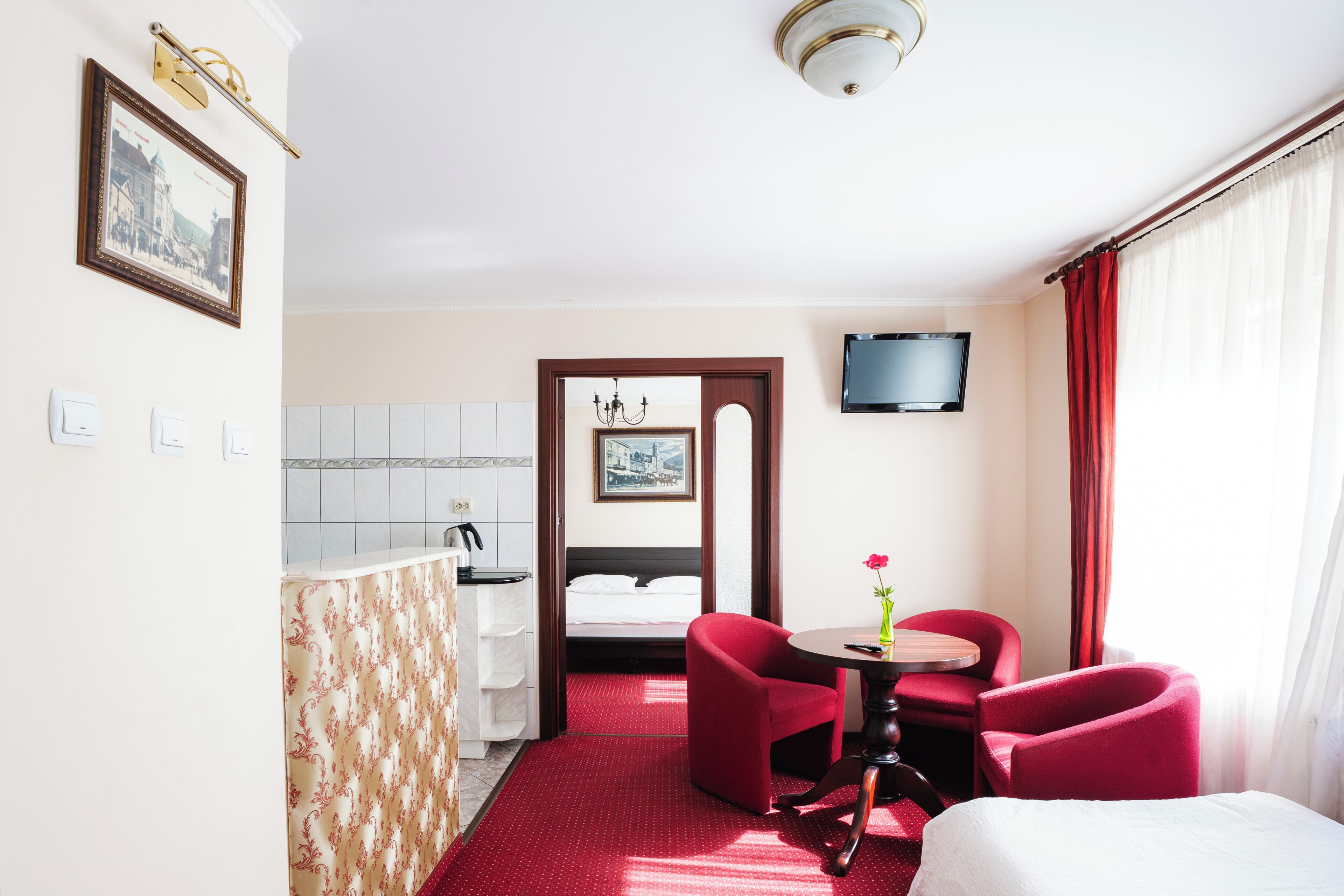 Une chambre d’hôtel avec un lit, un bureau et une chaise, une télévision et un rideau rouge.