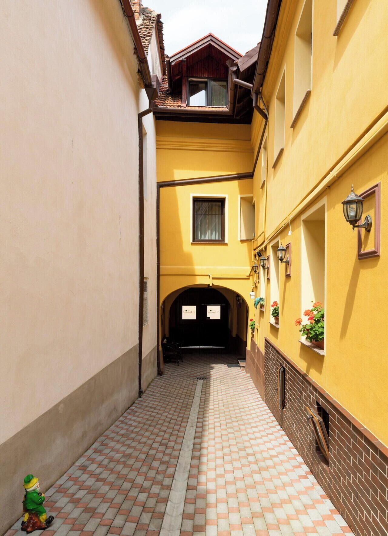 A narrow alleyway with a yellow building, a black door, and a small statue.