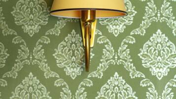 A wall-mounted lamp with a yellow shade against a green patterned wallpaper.