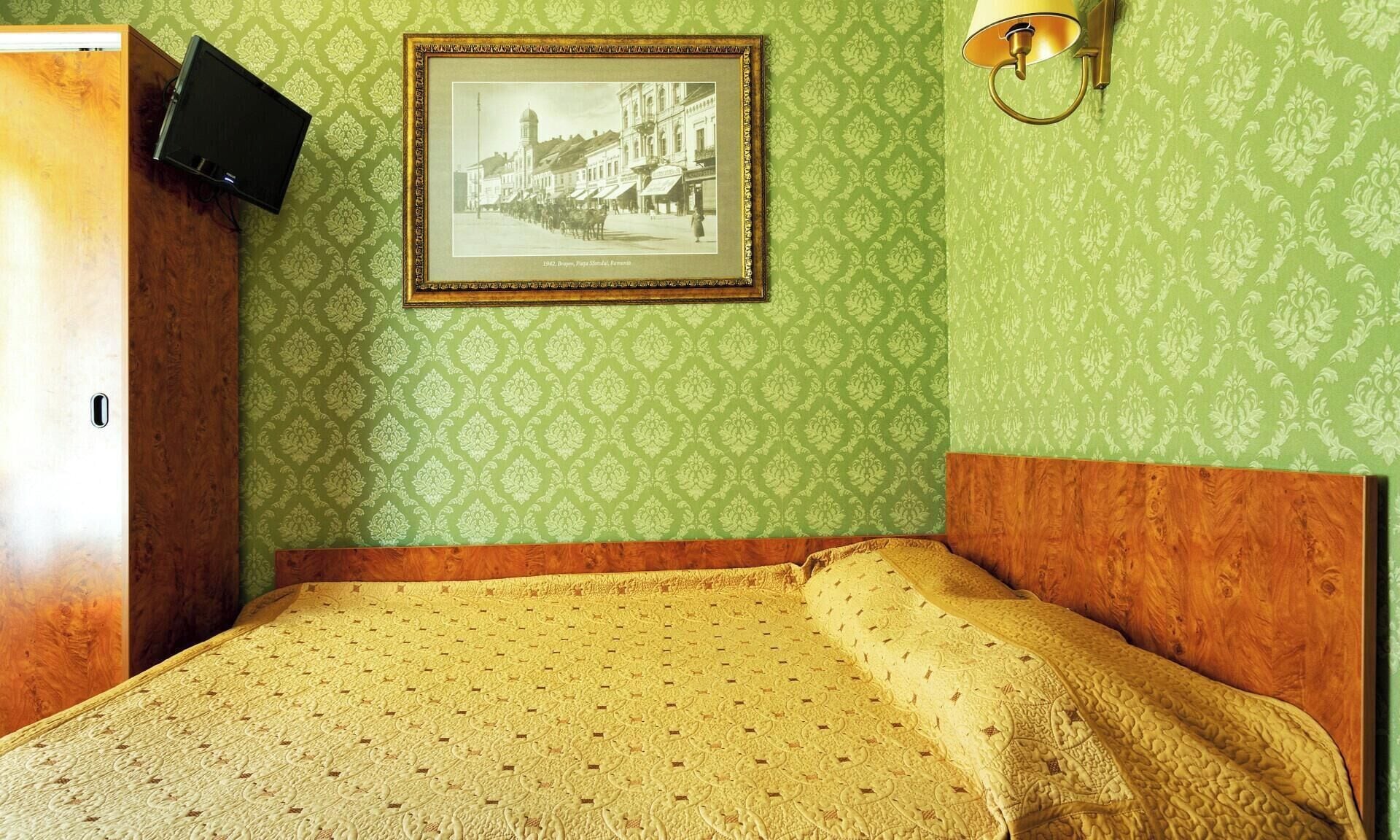 Una stanza con un letto, un quadro appeso al muro e una lampada fissata alla parete.