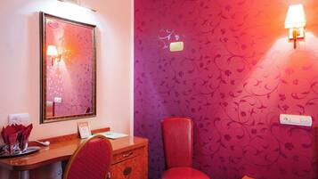 Une pièce avec un bureau en bois, une chaise rouge, un miroir et un mur recouvert d’un papier peint à motifs floraux.