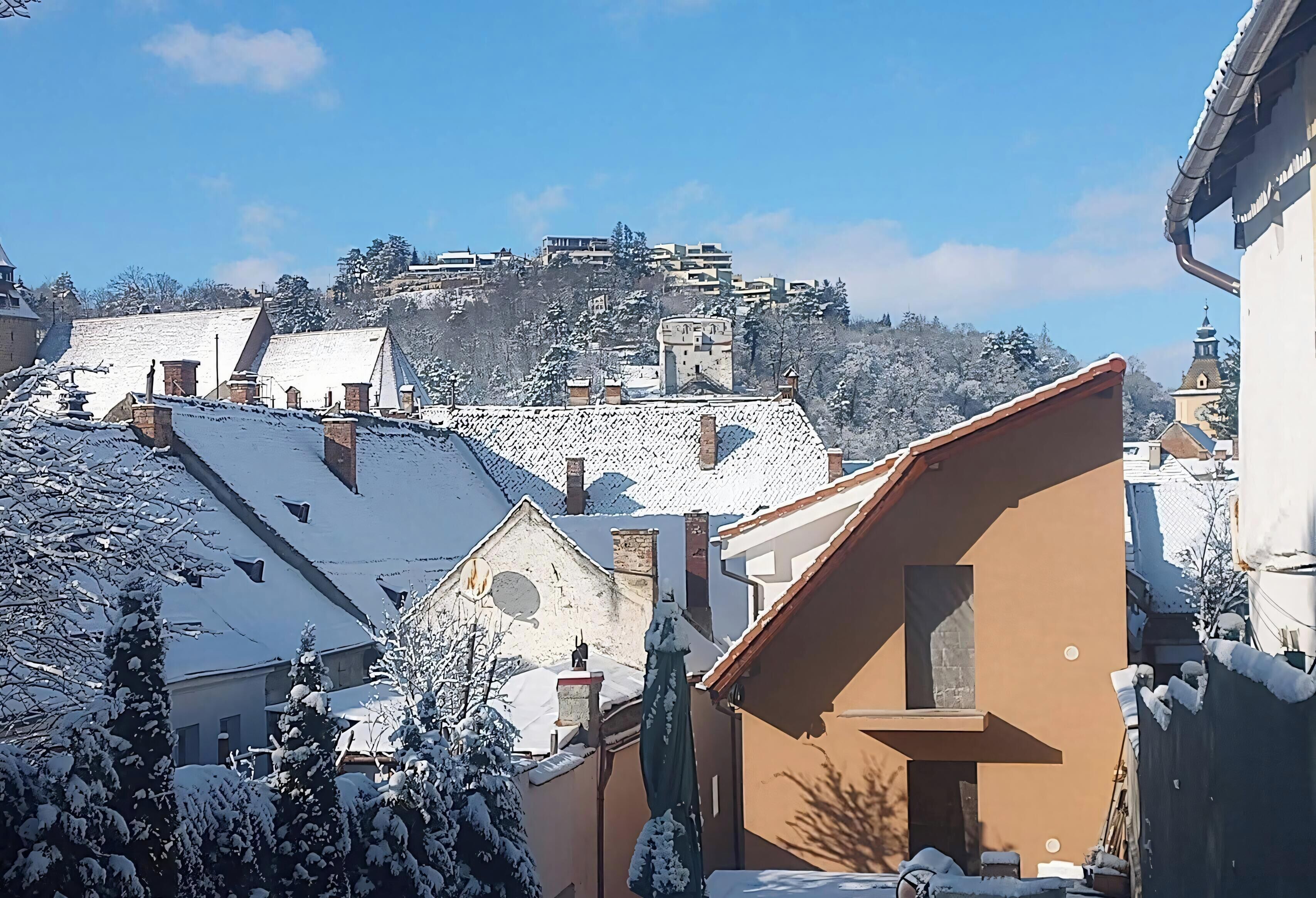A snowy residential area with buildings, including a prominent tower-like structure on a hill in the background.