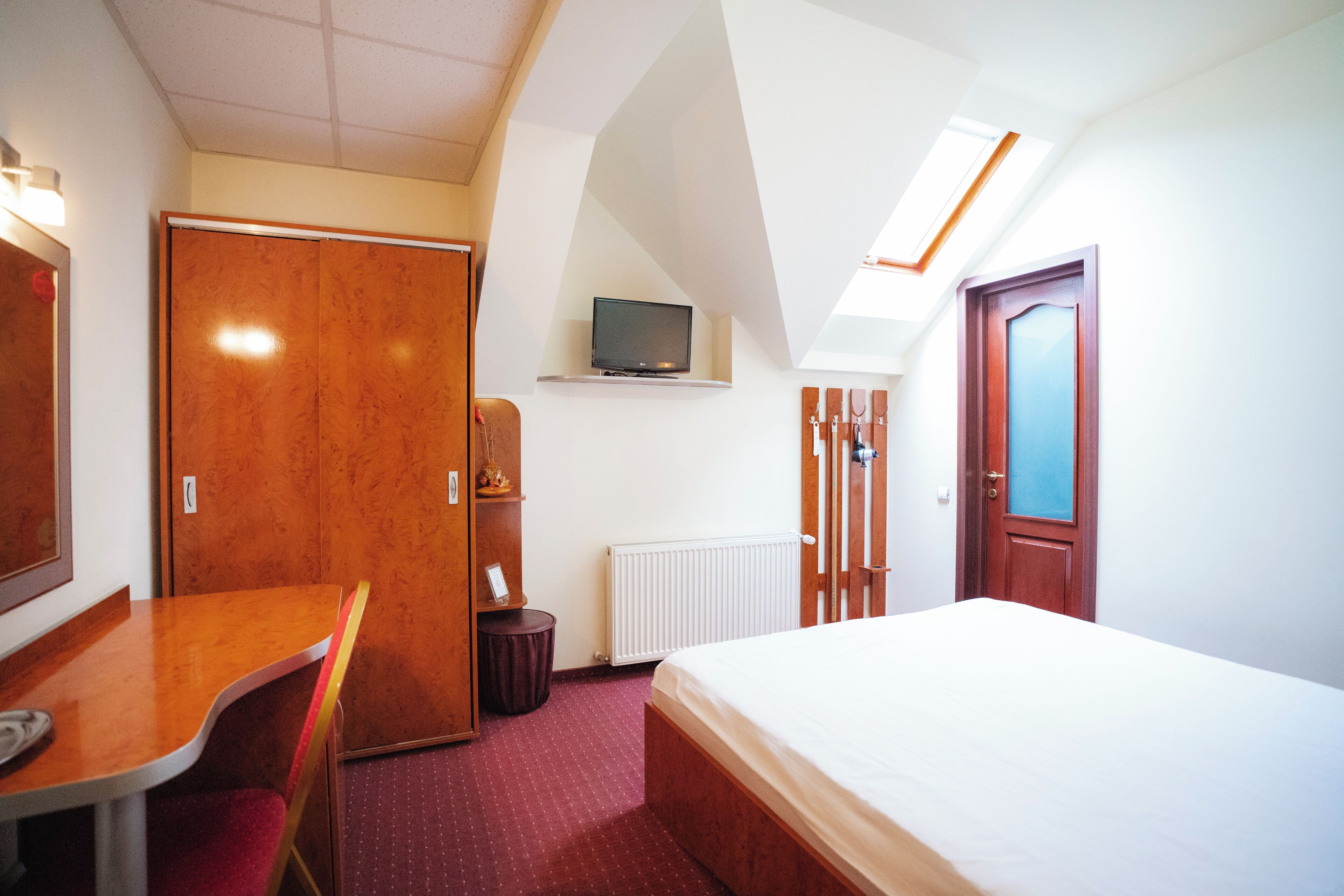Une chambre d’hôtel avec un lit, un bureau, une chaise, un téléviseur posé sur une étagère et une porte.