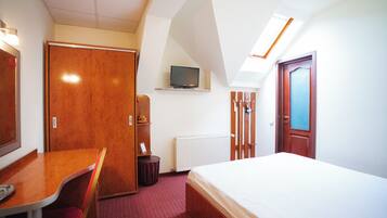 A hotel room with a bed, a desk, a chair, a television on a shelf, and a door.