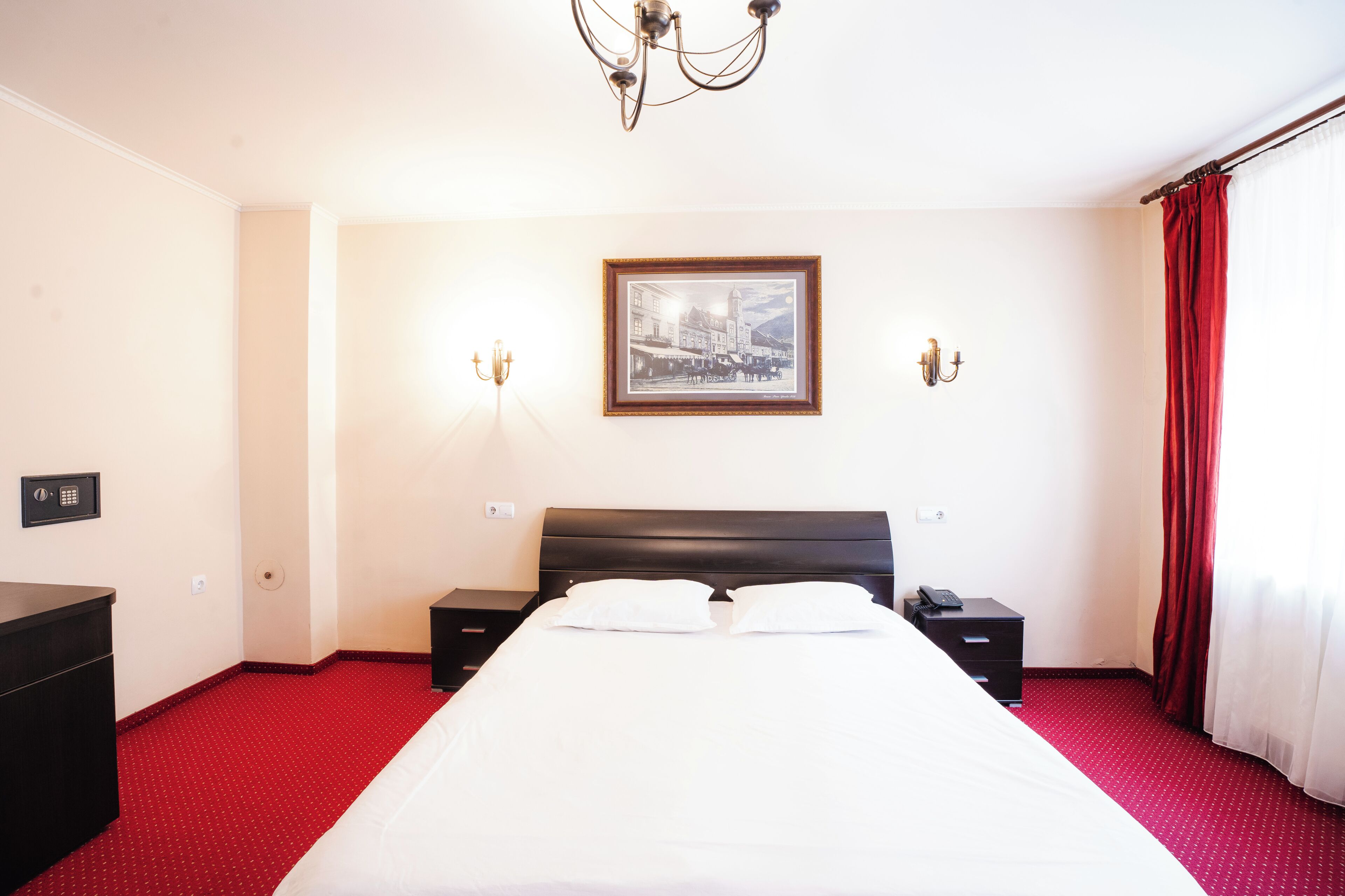 Une chambre d’hôtel avec un lit, des tables de chevet, une lampe, un tableau encadré au mur et une moquette rouge.
