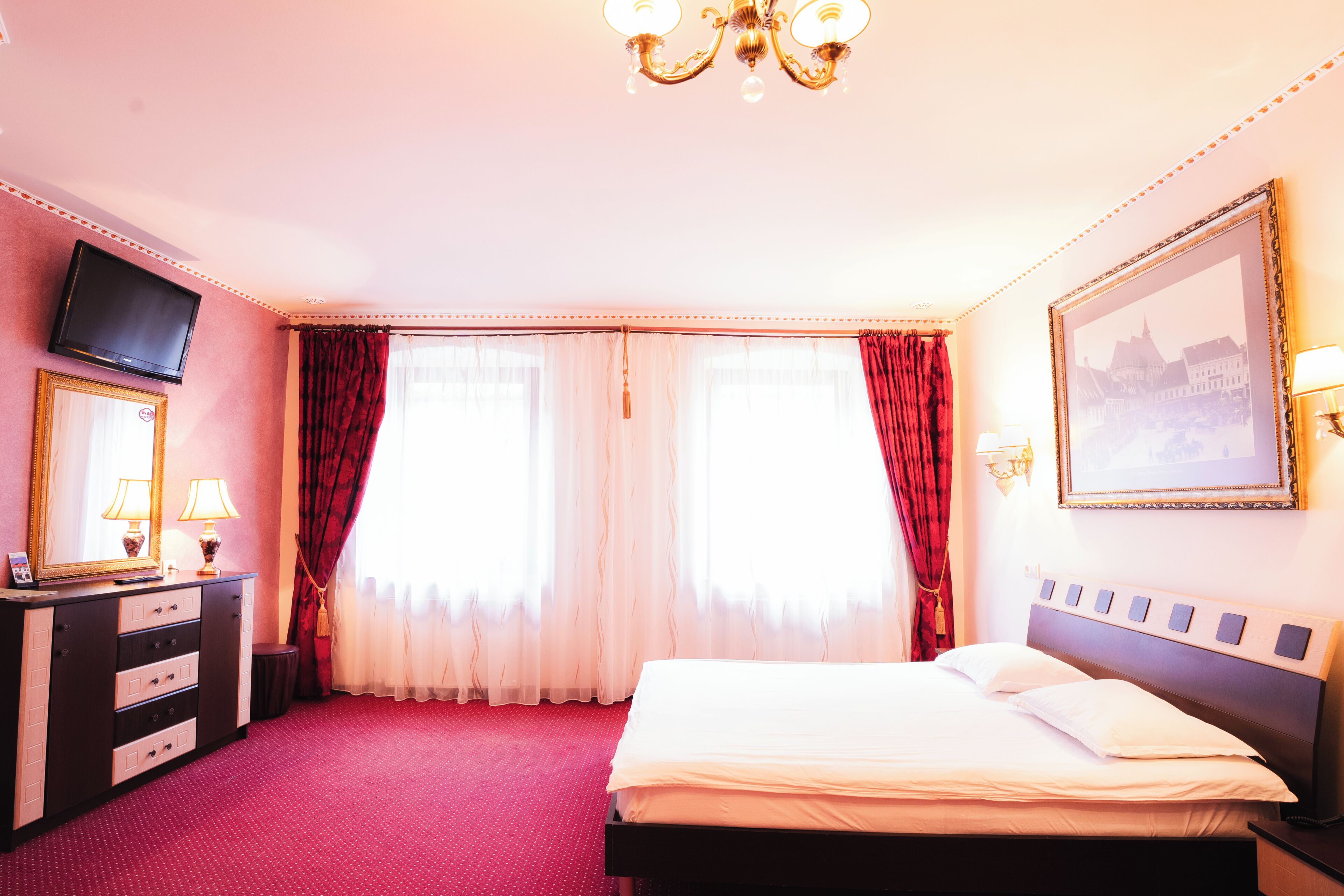 A hotel room with a bed, a TV, a dresser, and a painting on the wall.