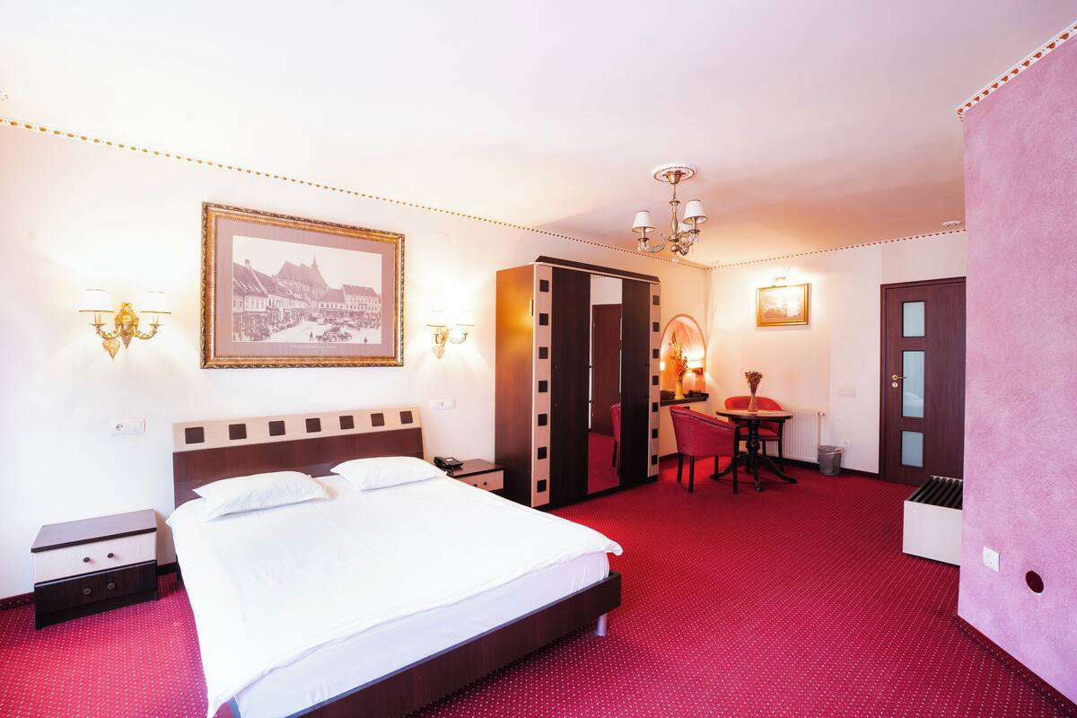 Habitación de hotel con una cama grande, un escritorio con silla, un espejo y un cuadro en la pared.