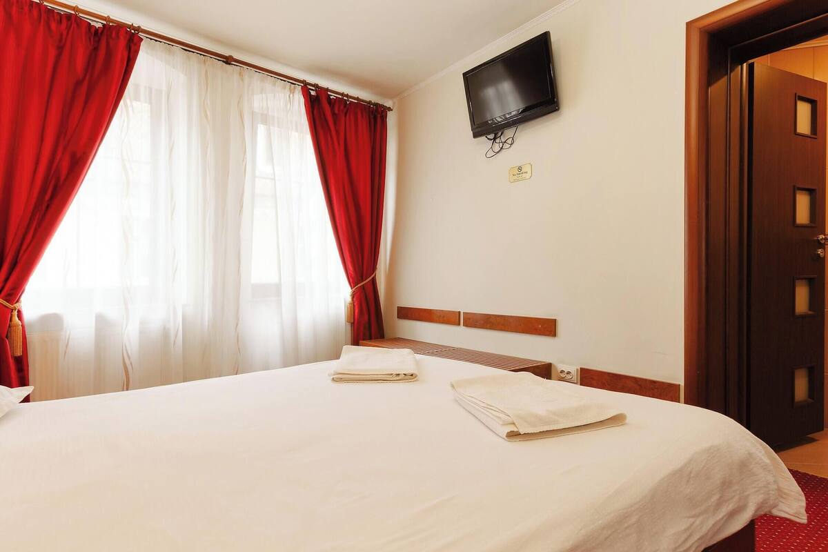 Una habitación de hotel con una cama, cortinas rojas, un televisor y una puerta de madera.