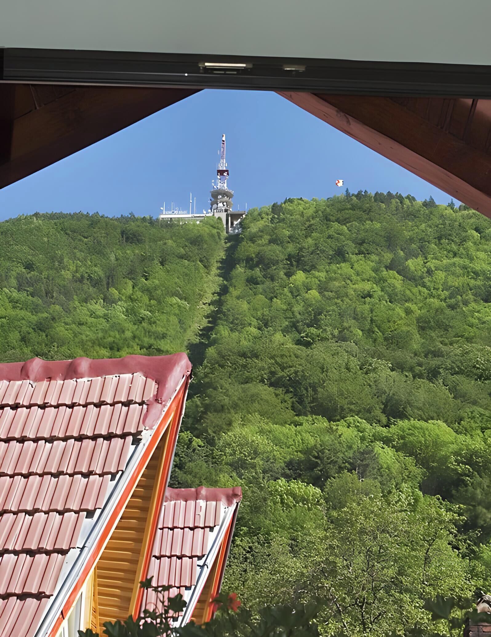 Vista desde un edificio con tejado rojo, mirando hacia abajo una colina a una torre con antenas.