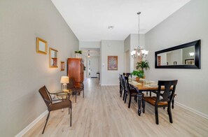 A dining area with a wooden table and chairs, a chandelier, and framed artwork on the walls. - Windsor Hills 4BR Single-Level Pool Home,By Disney (Kissimmee)