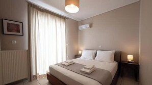 A hotel room with a bed, a nightstand, a window with curtains, an air conditioning unit, and a framed picture on the wall. - Chalandri Central Maisonette (Chalandri)