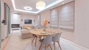 A modern dining area with a round table, grey chairs, and a chandelier. - Chalandri Central Maisonette (Chalandri)