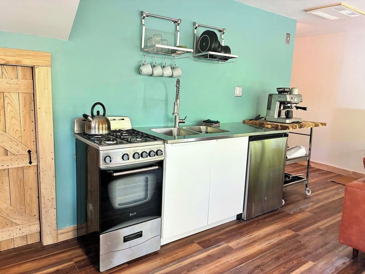 Cozinha compacta com fogão, forno e pia, piso de madeira e parede verde-água.