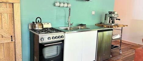Cozinha compacta com fogão, forno e pia, piso de madeira e parede verde-água.