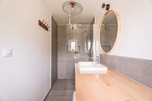 Un baño moderno con tocador de madera, un espejo grande y zona de ducha.