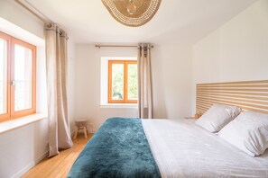 Un dormitorio con cama, cabecera de madera, ventana y un taburete pequeño.