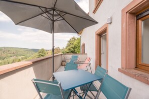Un balcón con una mesa, sillas y un paraguas grande, y vistas al paisaje.