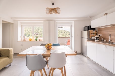 A modern kitchen with a dining area, large windows, and a view of the outdoors.. Apartment 'Chez Mémé' with Mountain View, Balcony and Wi-Fi