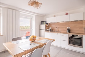 A modern kitchen with white cabinets, a wooden countertop, a built-in oven, and a dining area with a table and chairs.