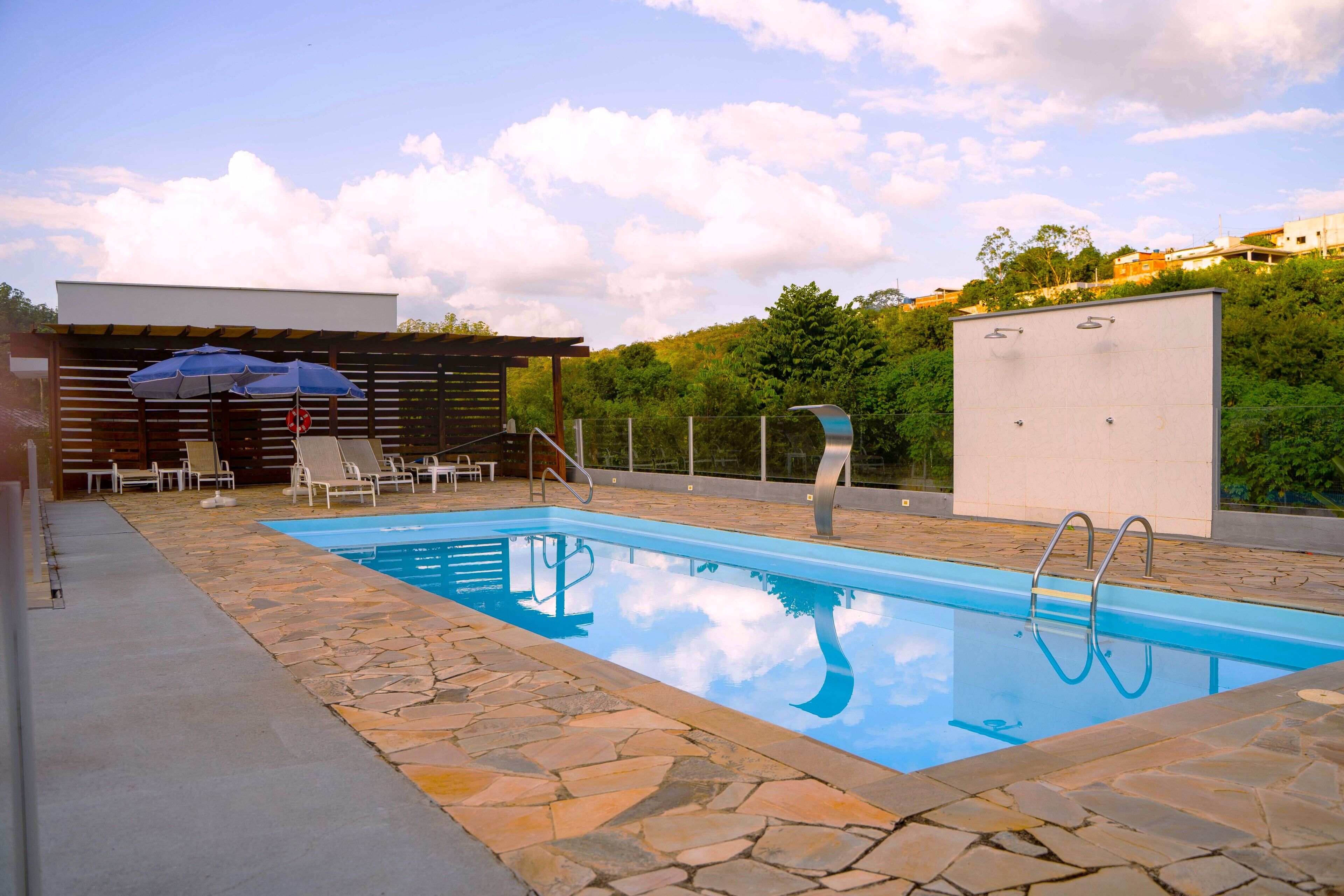 A swimming pool with stone tiles, lounge chairs, and a pergola with an umbrella.