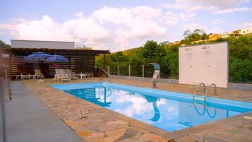 A swimming pool with stone tiles, lounge chairs, and a pergola with an umbrella.