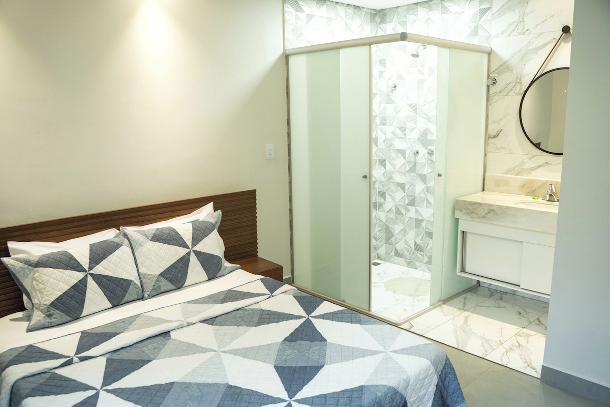Een slaapkamer met een bed, een nachtkastje, een badkamer met douche en een spiegel.