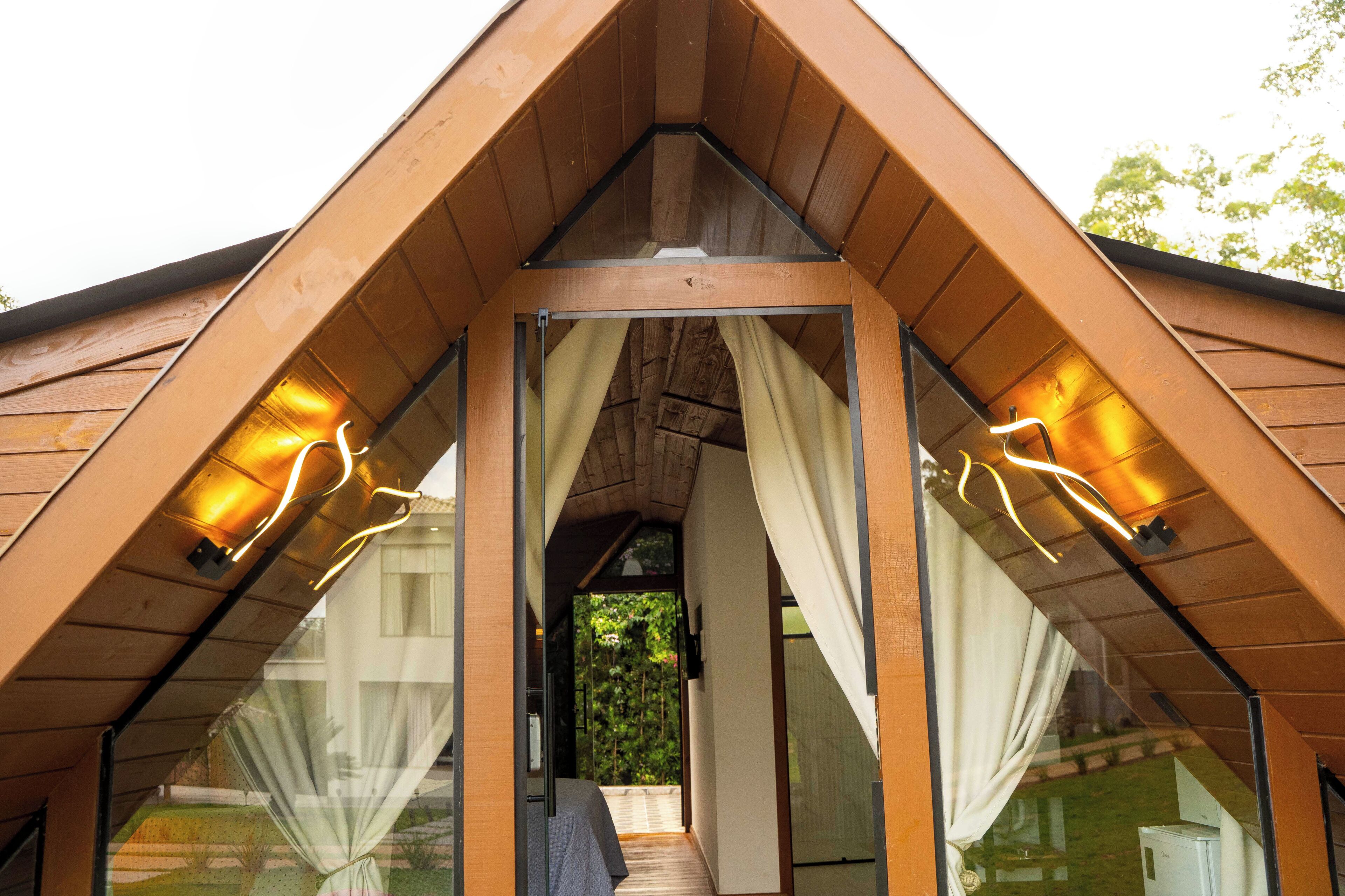 Una estructura de madera con techo triangular, puerta de vidrio y cortinas.