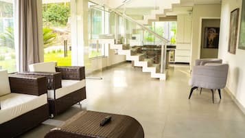 Un intérieur moderne avec un escalier menant à la cuisine, un coin repas avec des meubles en osier et un salon avec une télécommande posée sur une table.