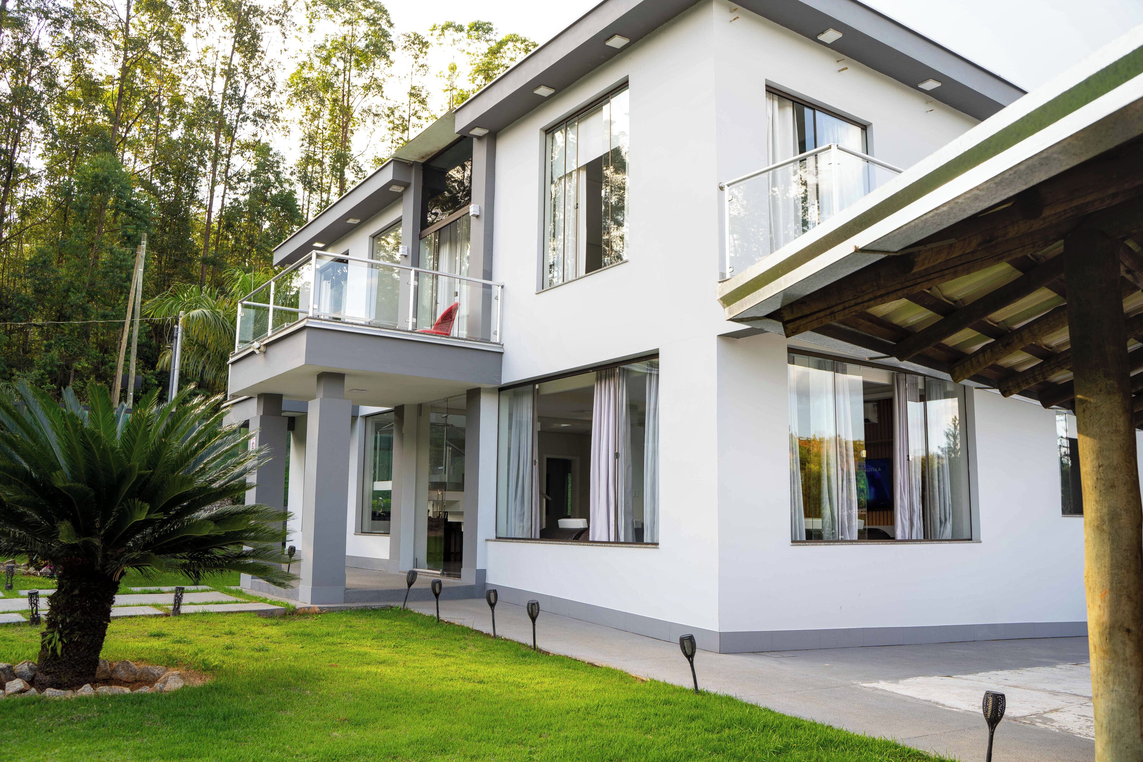 Uma casa moderna de dois andares com varanda, janelas amplas e gramado bem cuidado.