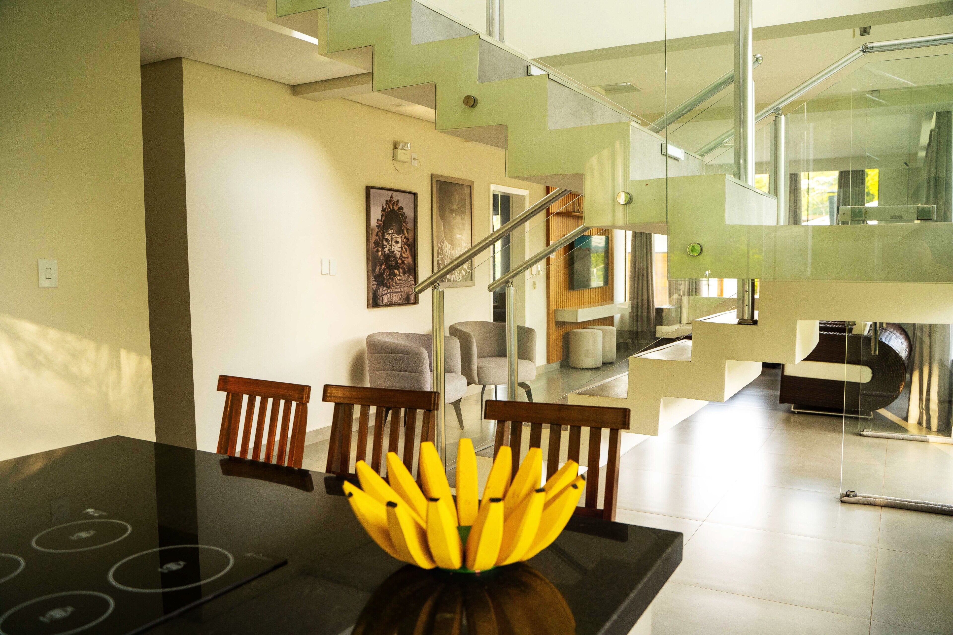 A modern interior with a dining table, chairs, a staircase, and a glass railing.