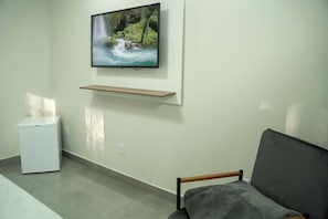 A room with a television mounted on the wall, a small white appliance, and a grey sofa.