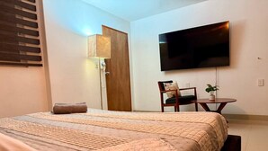 A hotel room with a bed, a desk, a chair, a TV, and a door.