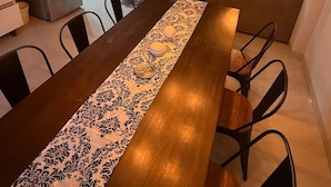 A dining area with a wooden table, patterned table runner, and hanging light fixtures.