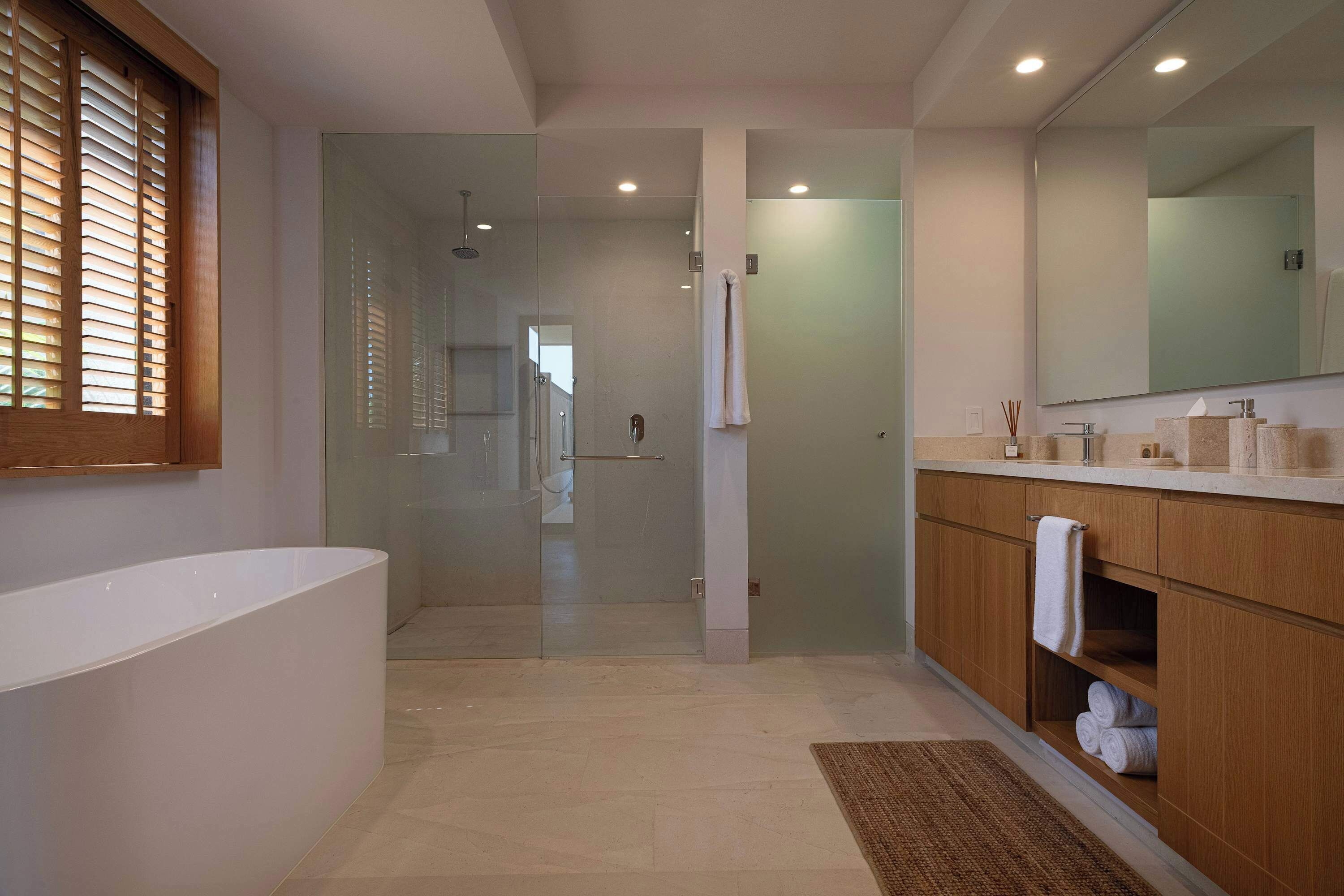 A modern bathroom with a glass-enclosed shower, a white bathtub, wooden cabinets, and a large mirror.