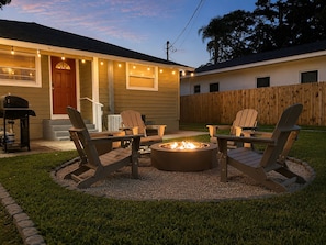Ein Garten mit Feuerstelle, Sitzgelegenheiten im Freien und einem Haus mit Lichterketten.