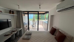 Quarto de hotel moderno com cama, televisão, escrivaninha com cadeiras e varanda com mesa e cadeiras.