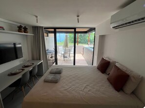 Ein modernes Hotelzimmer mit Bett, Fernseher, Schreibtisch mit Stühlen und einem Balkon mit Tisch und Stühlen.