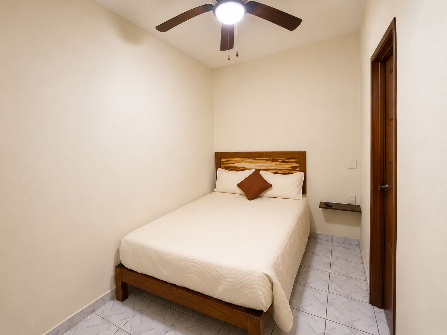 A bedroom with a bed, a ceiling fan, a wooden headboard, and a door.