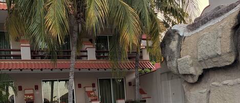 Una piscina con borde de azulejos, una palmera y un edificio con balcón.